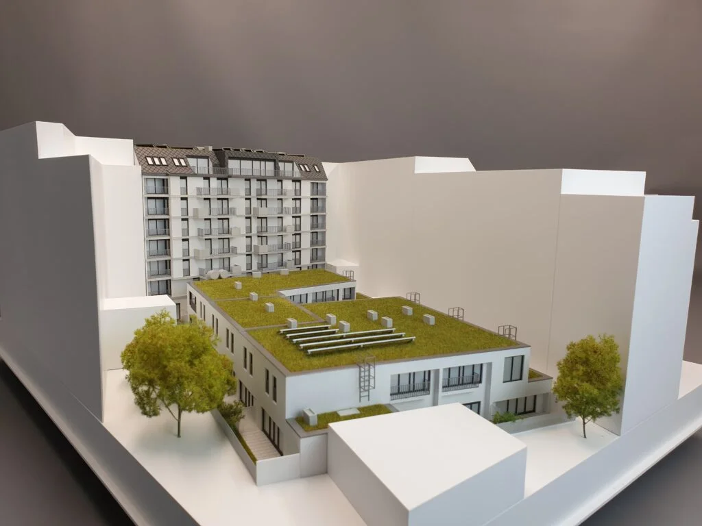 Architekturmodell Stadtblock 1:100 – Innenhof mit begrünten Flachdächern, Umgebungsbauten und Bäumen.