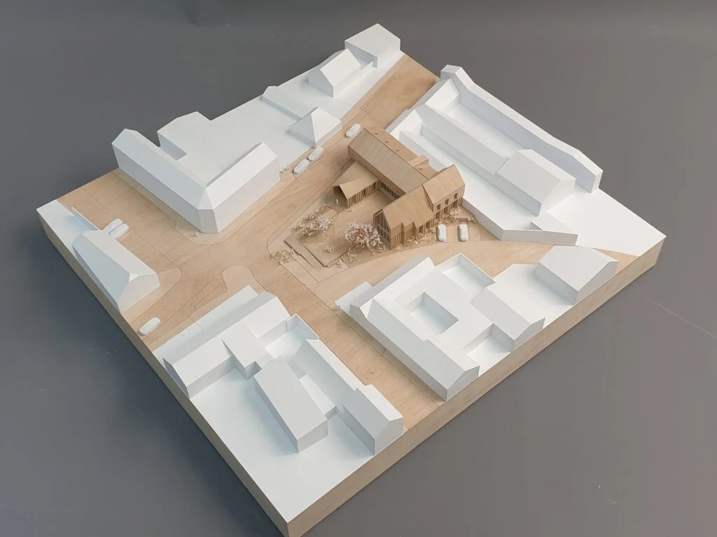 Umgebungsmodell 1:500 – Dorfkern mit abstrahierten Gebäuden in Weiß, Holzvolumen für den Entwurf, Straßen und Bepflanzung.