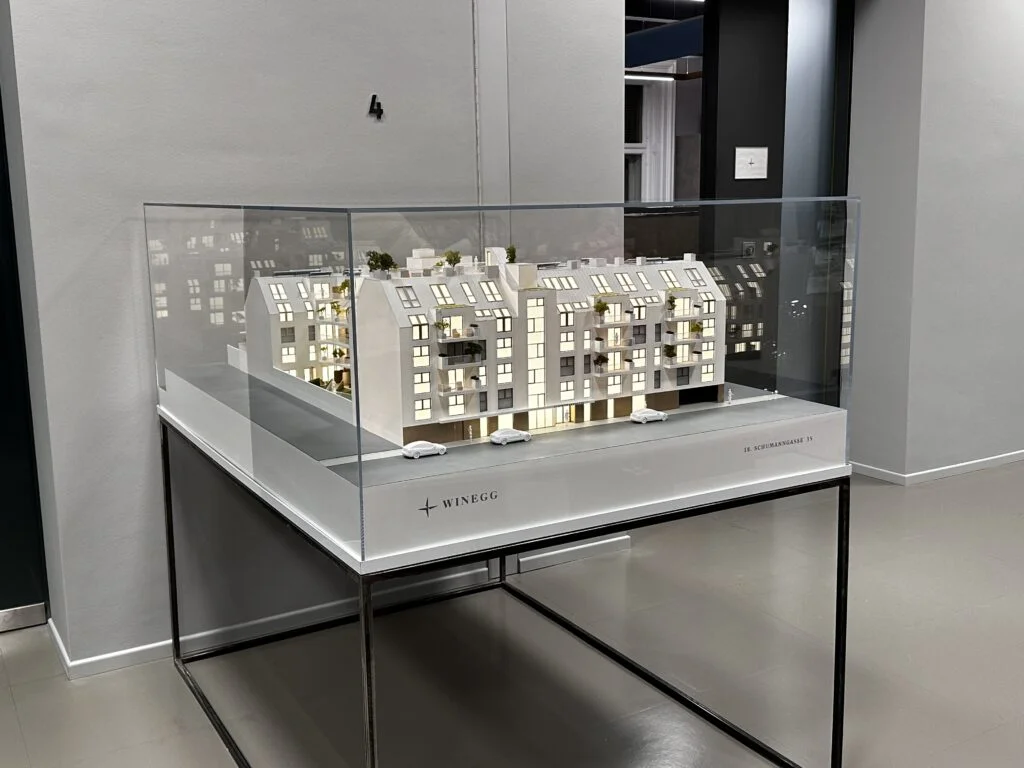Architekturmodell Immobilien 1:100 – Wohnhaus mit beleuchteten Wohnungen in Acrylglasvitrine.