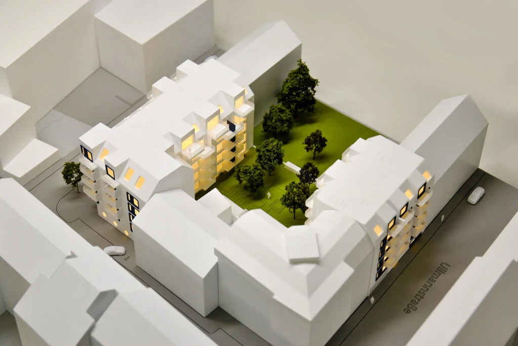 Architekturmodell Wohnhaus 1:200 – moderne Wohnanlage mit Innenhof, Grünflächen, Bäumen und beleuchteten Gebäudeteilen.