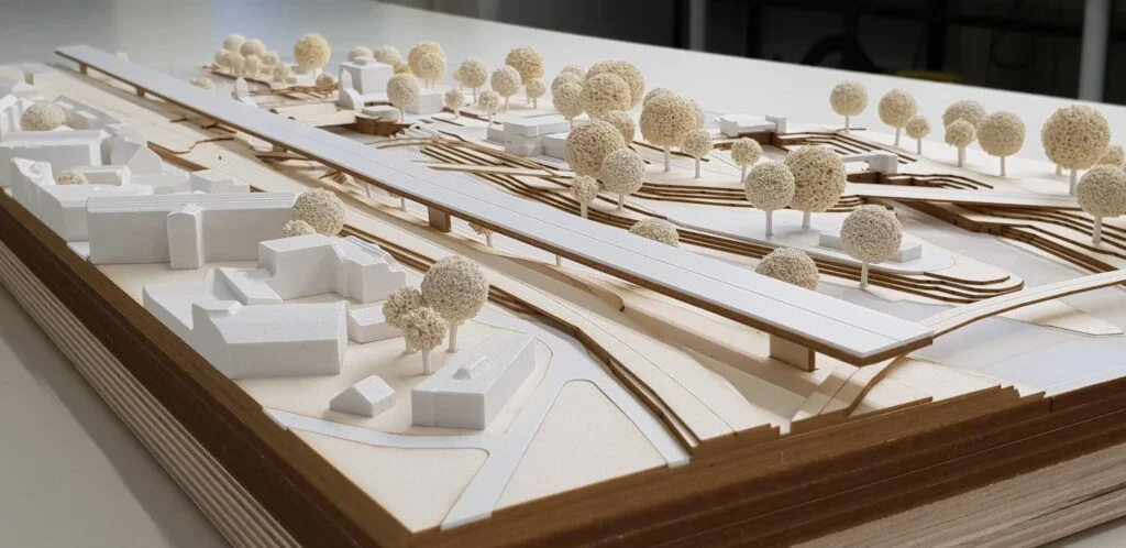 Wettbewerbsmodell 1:500 – Infrastrukturprojekt mit Brücke, Straßen und umgebenden Gebäuden, mit Bäumen dargestellt.