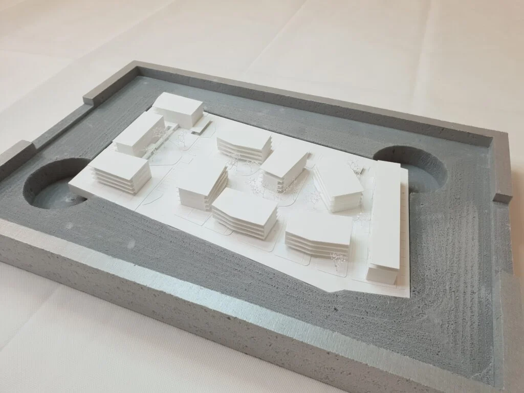 Wettbewerbsmodell 1:500 – Wohnanlage mit mehreren Baukörpern, integriert in einen grauen Betonrahmen.
