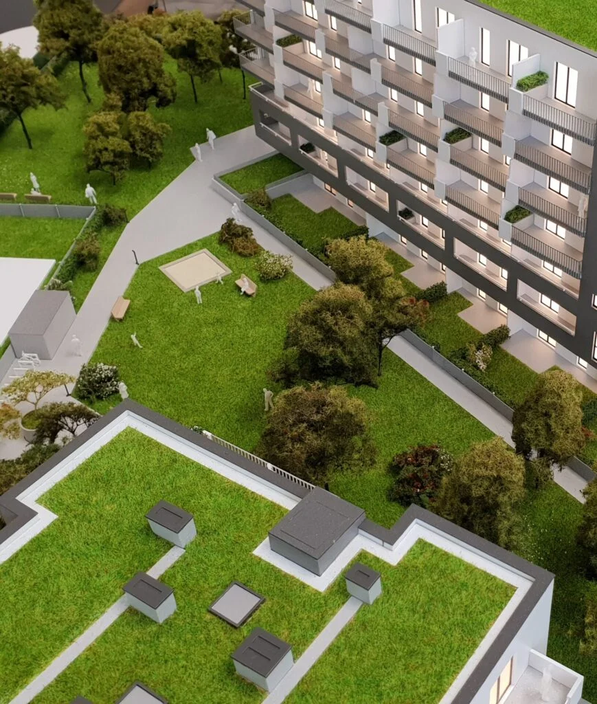 Architekturmodell 1:100 – Wohnhaus mit Innenhof, Grünflächen, Spielplatz und Dachgärten, detailreich und beleuchtet dargestellt.