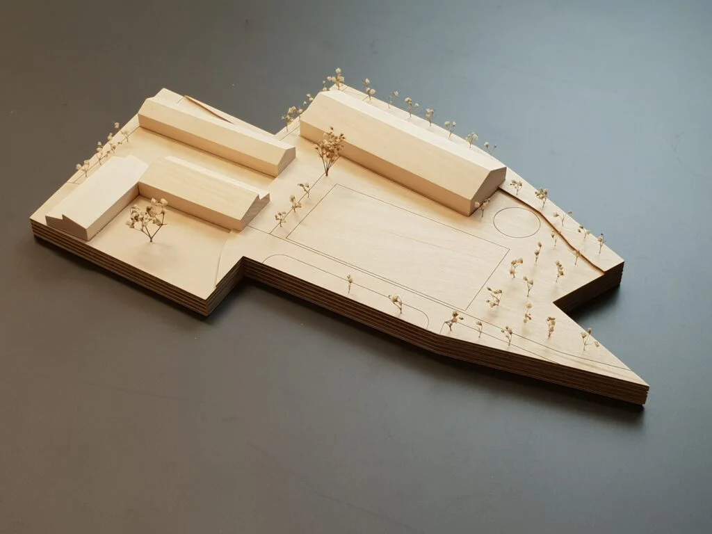 Architekturmodell aus Holz – reduziertes Umgebungsmodell mit Gebäudeblöcken, Bäumen und Spielfeld.