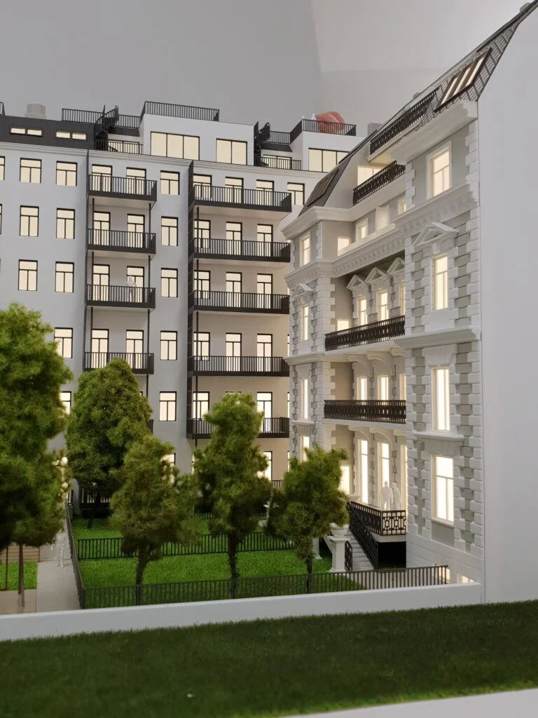 Immobilienmodell einer Wohnanlage im Maßstab 1:100 – Innenhof mit Bäumen, Fassadendetails und beleuchteten Wohnungen