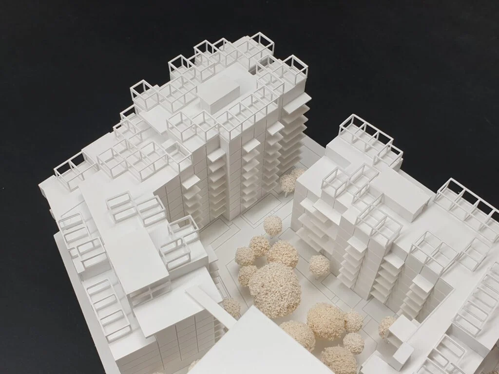 Architekturmodell – Wettbewerbsmodell im Maßstab 1:500, weißes Wohngebäudemodell mit Balkonstrukturen, klarer Geometrie und integrierter Begrünung mit Bäumen.