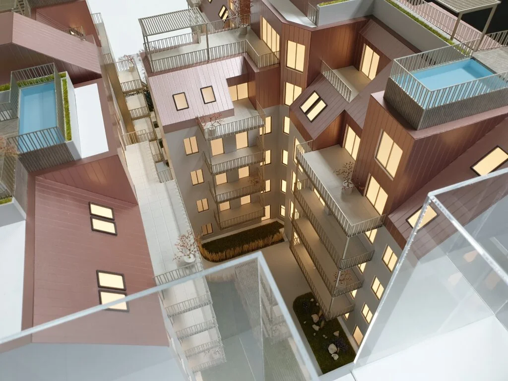 Architekturmodell Wohnhausanlage mit Innenhof, Dachterrassen, Pools und beleuchteten Fassaden.
