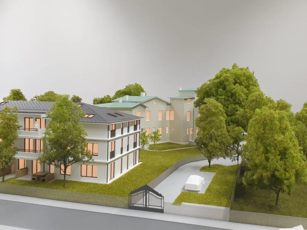 Architekturmodell 1:100 – Wohnanlage mit zwei Gebäuden, Gartenflächen, Bäumen und Zufahrt, realistisch und detailreich dargestellt.