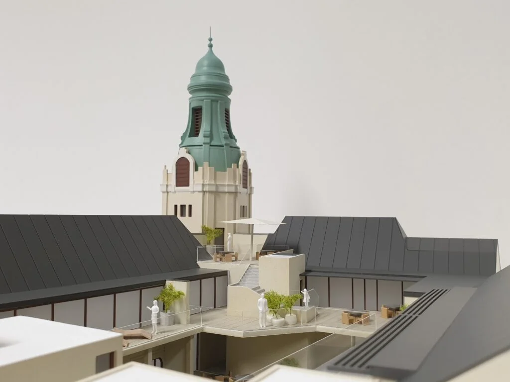 Architekturmodell 1:100 – Wohnhaus mit modernen Dachterrassen und historischem Kirchturm im Hintergrund, realistisch gestaltet.