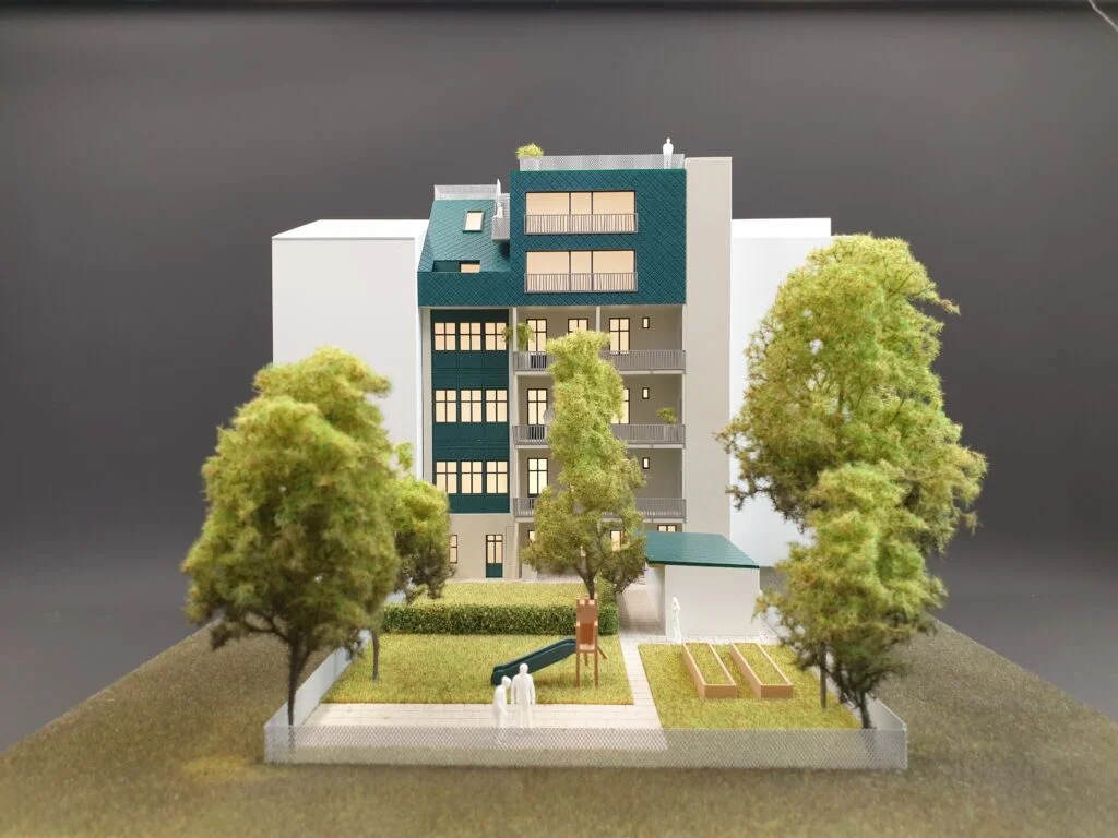 Architekturmodell Mehrfamilienhaus mit Garten, Bäumen und Spielplatz im Maßstab 1:100.