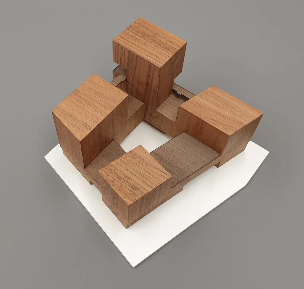 Architekturmodell aus Holz – minimalistische Baukörper als Quader, platziert auf weißem Sockel.