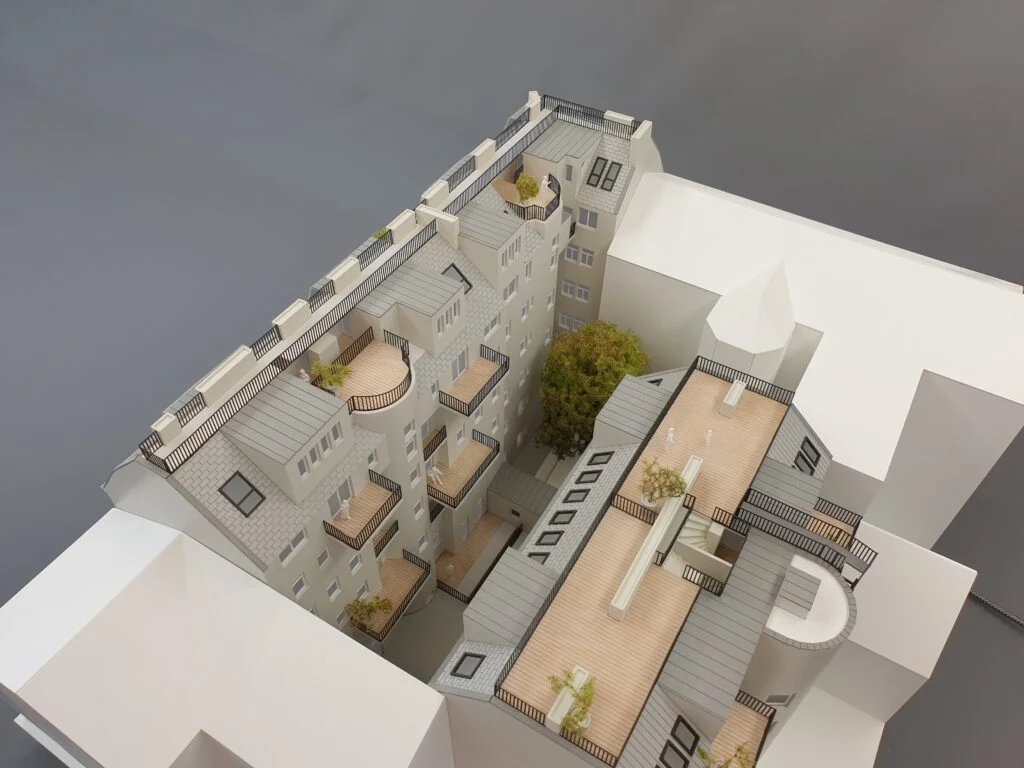 Architekturmodell eines Wohnhauses mit Innenhof, Dachterrassen und begrünten Bereichen, detailgetreu umgesetzt.