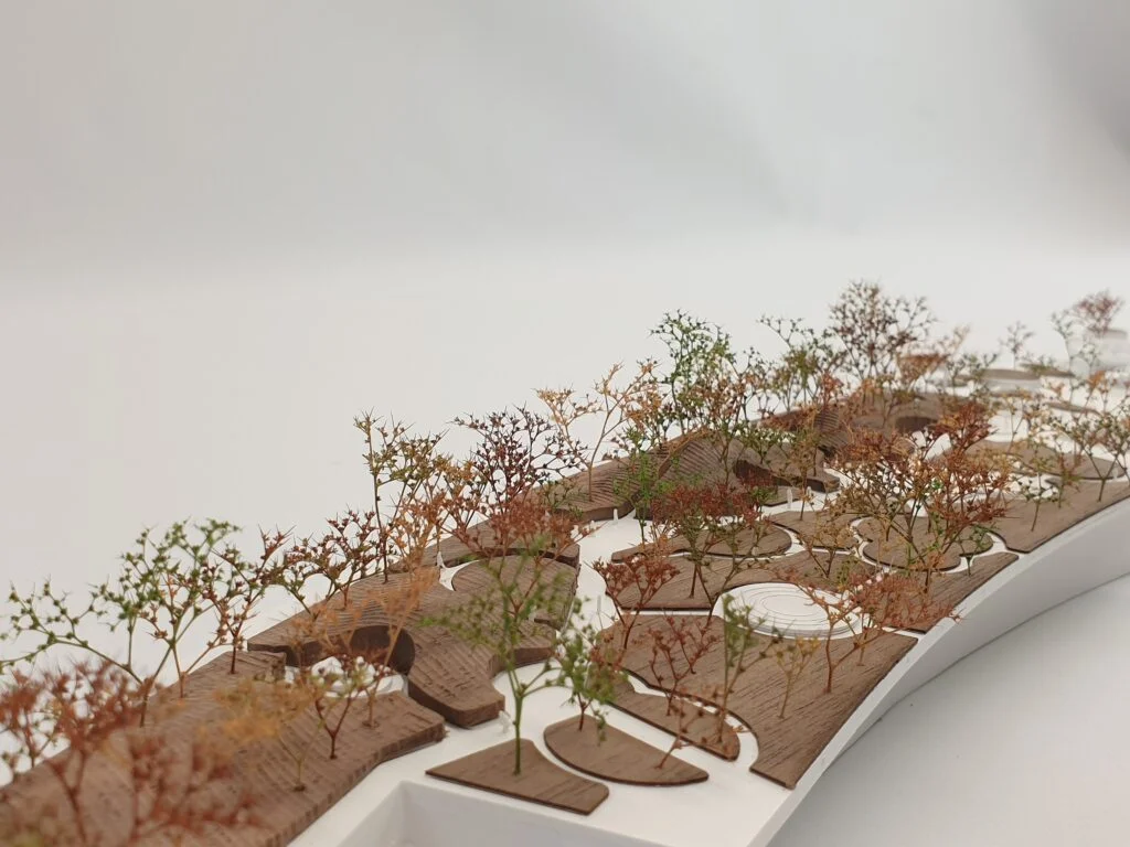 Architekturmodell Landschaft – Holzflächen mit bunten Bäumen und weißen Wegen, abstrahierte Darstellung von Grünanlagen.