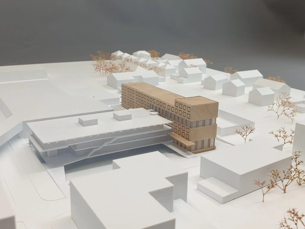 Architekturmodell Wohnkomplex – Holz- und Weißmodell mit umliegender Bebauung und Bäumen für städtebauliche Planung.