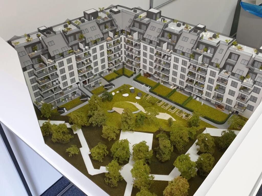 Vollfarbiges Architekturmodell – Wohnanlage mit großem Innenhof, Spielplatz, Balkonen und Grünflächen.