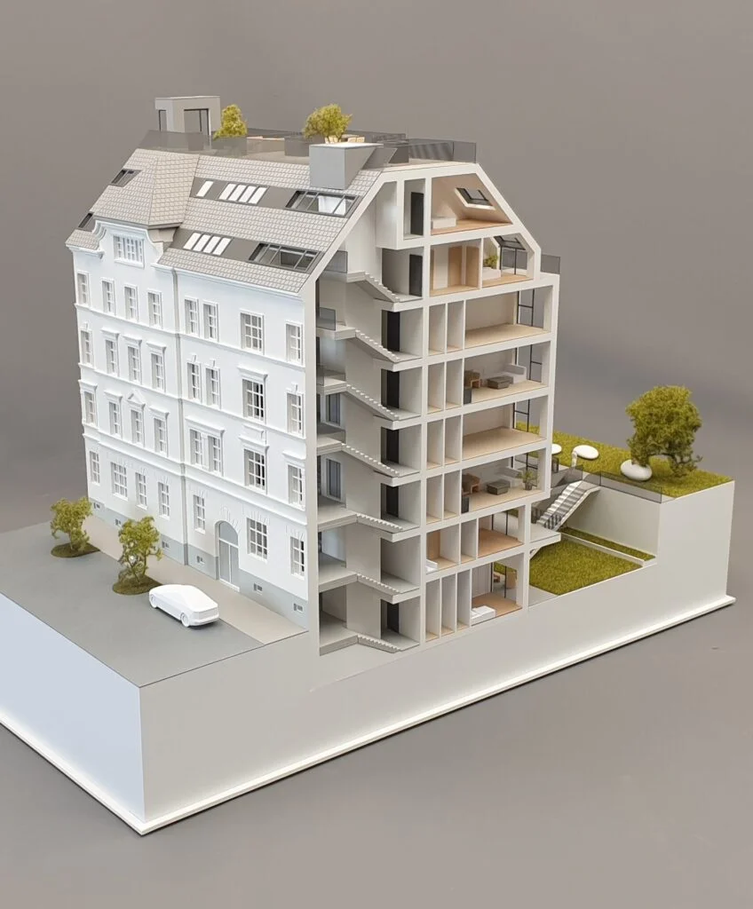 Architekturmodell – Schnittmodell eines mehrstöckigen Wohnhauses im Maßstab 1:100, mit detaillierten Innenräumen, Einrichtung, Treppenhäusern und begrüntem Hofbereich.