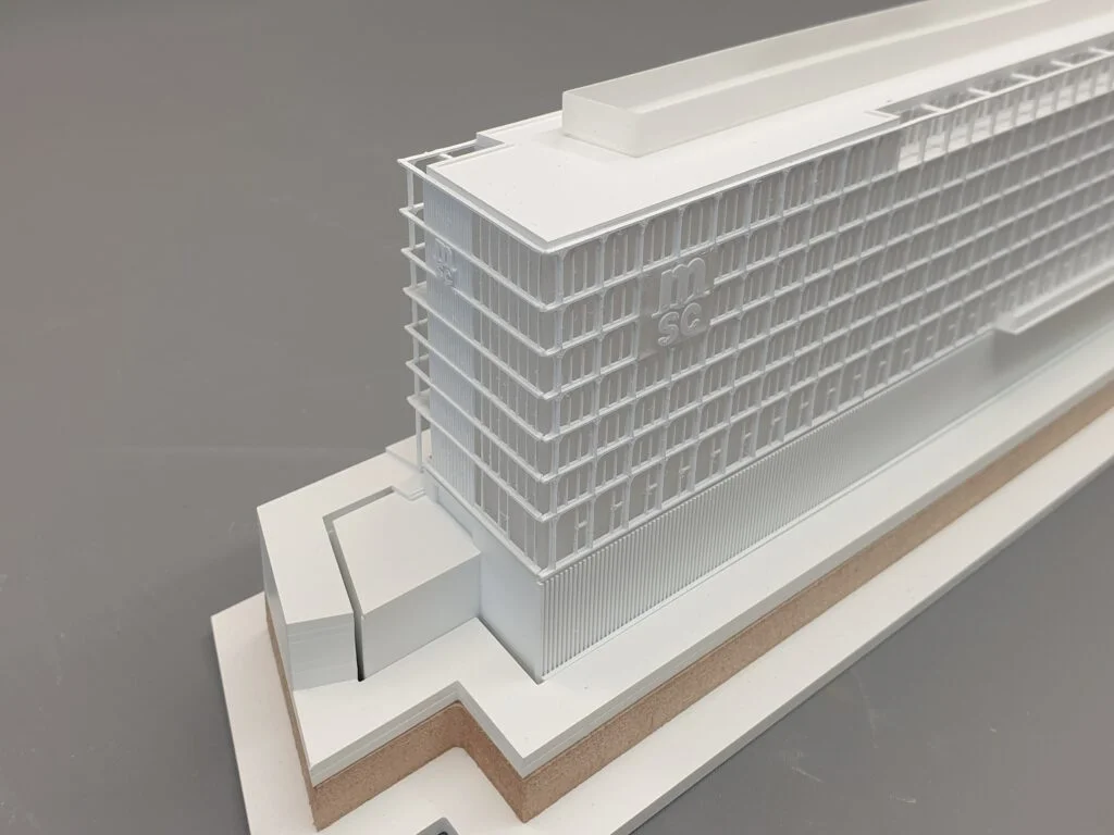 Architekturmodell im Maßstab 1:500 – Wettbewerbsmodell eines modernen Hochhauses mit klarer Fassadenstruktur und Firmenlogo.