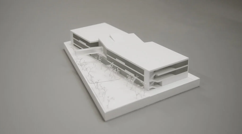 Wettbewerbsmodell 1:500 – moderner Bildungsbau mit klarer Geometrie, offenen Fassaden und Baumgruppen im Umfeld.