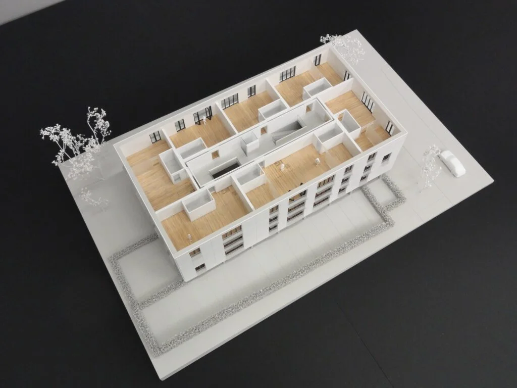 : Architekturmodell Funktionsmodell Wohnhaus mit sichtbarem Grundriss, Holzböden und abstrahiertem Außenbereich mit Bäumen. (