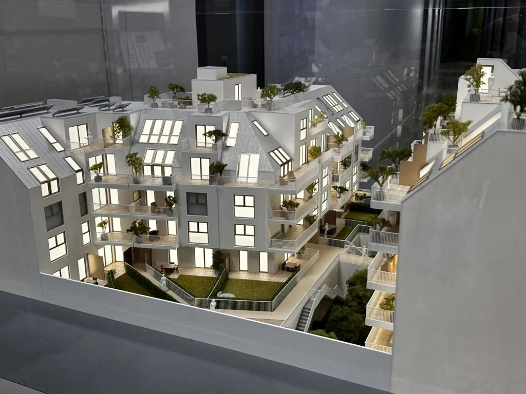 Architekturmodell 1:50/1:75 – beleuchtete Wohnanlage mit Balkonen, Dachterrassen, Grünflächen und moderner Architektur.
