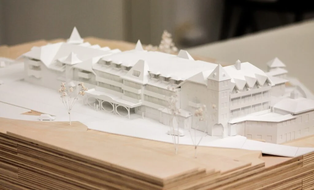 Architekturmodell Hotel 1:200 – weiße Gebäudemodelle mit Holz-Topografie, abstrahierte Landschaft und präzise handgefertigte Details.