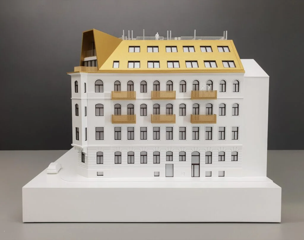 Architekturmodell 1:100 – Wohnhaus mit Innenhof, Grünflächen, Spielplatz und Dachgärten, detailreich und beleuchtet dargestellt.