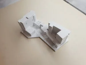 Weißes 3D-Druck Architekturmodell eines Wohnkomplexes mit mehreren Gebäuden und Innenhof, auf hellem Hintergrund präsentiert.