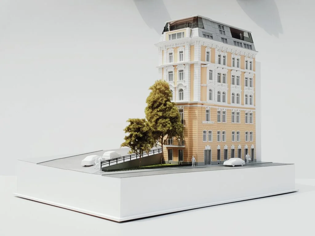 Architekturmodell – farbiges Wiener Eckhaus mit Bäumen, Straßenraum und Fahrzeugen, detailgetreu dargestellt.
