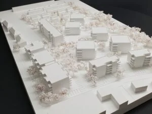 Weißes 3D-Druck Modell mit mehreren Wohngebäuden und Bäumen, städtebauliches Konzept einer Wohnanlage auf rechteckiger Grundplatte.