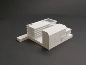 Weißes 3D-Druck Modell eines modernen Gebäudes mit abgestufter Kubatur und Fassadendetails, auf dunklem Hintergrund präsentiert.