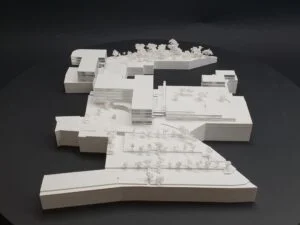 Weißes 3D-Druck Modell mit umfangreicher städtebaulicher Struktur, Gebäuden, Straßen und Bäumen, auf dunklem Hintergrund präsentiert.