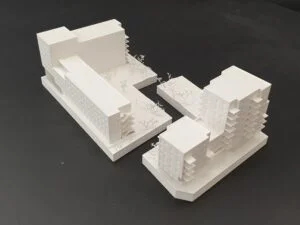Weißes 3D-Druck Modell mit mehreren Wohngebäuden in Blockstruktur, Fassadengliederung und Bäumen, auf dunklem Hintergrund.