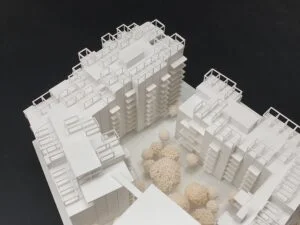 Weißes 3D-Druck Modell mehrerer Wohngebäude mit sichtbaren Fassadendetails und Bäumen im Innenhof, auf dunklem Hintergrund.