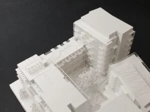 Weißes 3D-Druck Modell eines Wohnblocks mit klarer Fassadengliederung und Innenhof mit Begrünung, auf dunklem Hintergrund präsentiert.