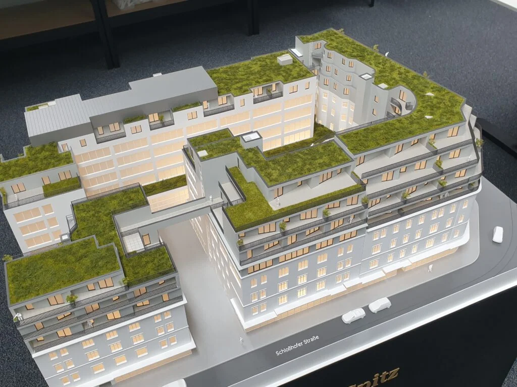 Immobilienmodell im Maßstab 1:200 – moderner Wohnkomplex mit begrünten Dachflächen, Balkonen und beleuchteten Innenhöfen.