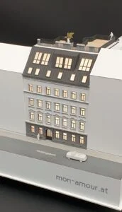 Immobilienmodell eines Wohnhauses im Maßstab 1:200 – saniertes Gebäude mit Dachterrasse und beleuchteten Wohnungen.