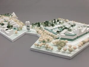 Weißes 3D-Druck Städtebaumodell mit Gebäuden, Grünflächen und vielen Bäumen, auf rechteckiger Grundplatte präsentiert.