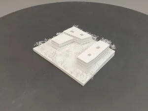 Weißes 3D-Druck Modell mit drei Gebäuden und Bäumen, rechteckige Anordnung auf Grundplatte, präsentiert auf dunklem Hintergrund.