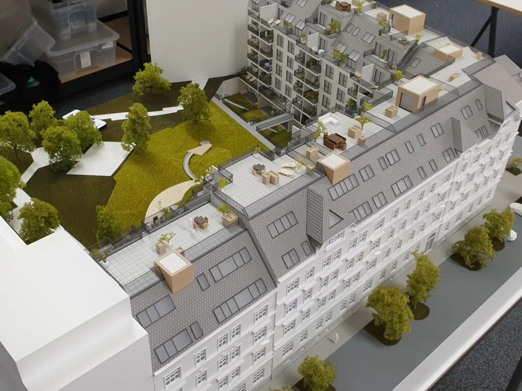 Architekturmodell Wohnanlage – großes Gebäudeensemble mit Dachterrassen, Grünflächen, Innenhof und Bäumen.