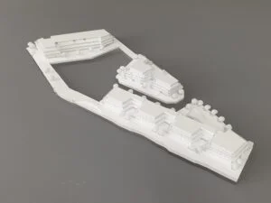 Weißes 3D-Druck Modell mit mehreren Gebäuden, Straßenführung und Begrünung, präsentiert auf grauem Hintergrund.