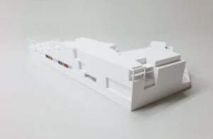 Weißes 3D-Druck Modell eines modernen Gebäudes mit klarer Kubatur und farbigen Fassadendetails auf heller Fläche.