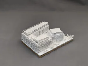 Weißes 3D-Druck Modell eines modernen Gebäudekomplexes mit mehreren Baukörpern und Bäumen, auf rechteckiger Grundplatte.