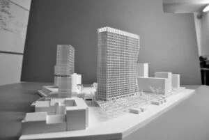 Weißes 3D-Druck Modell mit markantem Hochhaus und umliegenden Gebäuden, städtebauliches Konzept auf Grundplatte.