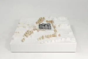 Gelände- und Umgebungsmodell in Weiß mit zentralem grauem Baukörper und Baumgruppen im Maßstab 1:500, frontal aufgenommen.