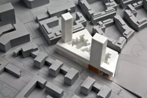 Städtebauliches Ausstellungsmodell mit weißen Bestandsvolumen und zwei weißen Hochpunkten auf grauem Stadtblock.