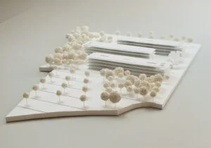 Wettbewerbsmodell mit langgestreckten Gebäuderiegeln und dichter Baumlandschaft in Weiß, Ansicht schräg von vorne.