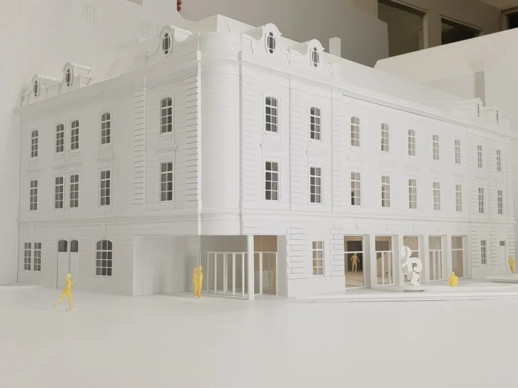 Weißes Ausstellungsmodell eines historischen Gebäudes mit Fassade und gelben Figuren im Vordergrund, Wettbewerbsmodell