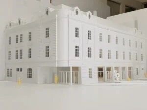 Weißes Ausstellungsmodell eines historischen Gebäudes mit Fassade und gelben Figuren im Vordergrund, Wettbewerbsmodell