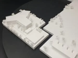Wettbewerbsmodell mit Schulgebäude und Sportanlagen im weißen Architekturmodell, Maßstab 1:500, klare Volumina und Bäume.