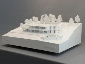 Weißes Architekturmodell eines modernen Hauses auf Hanglage mit detaillierter Topografie und umliegenden weißen Bäumen.